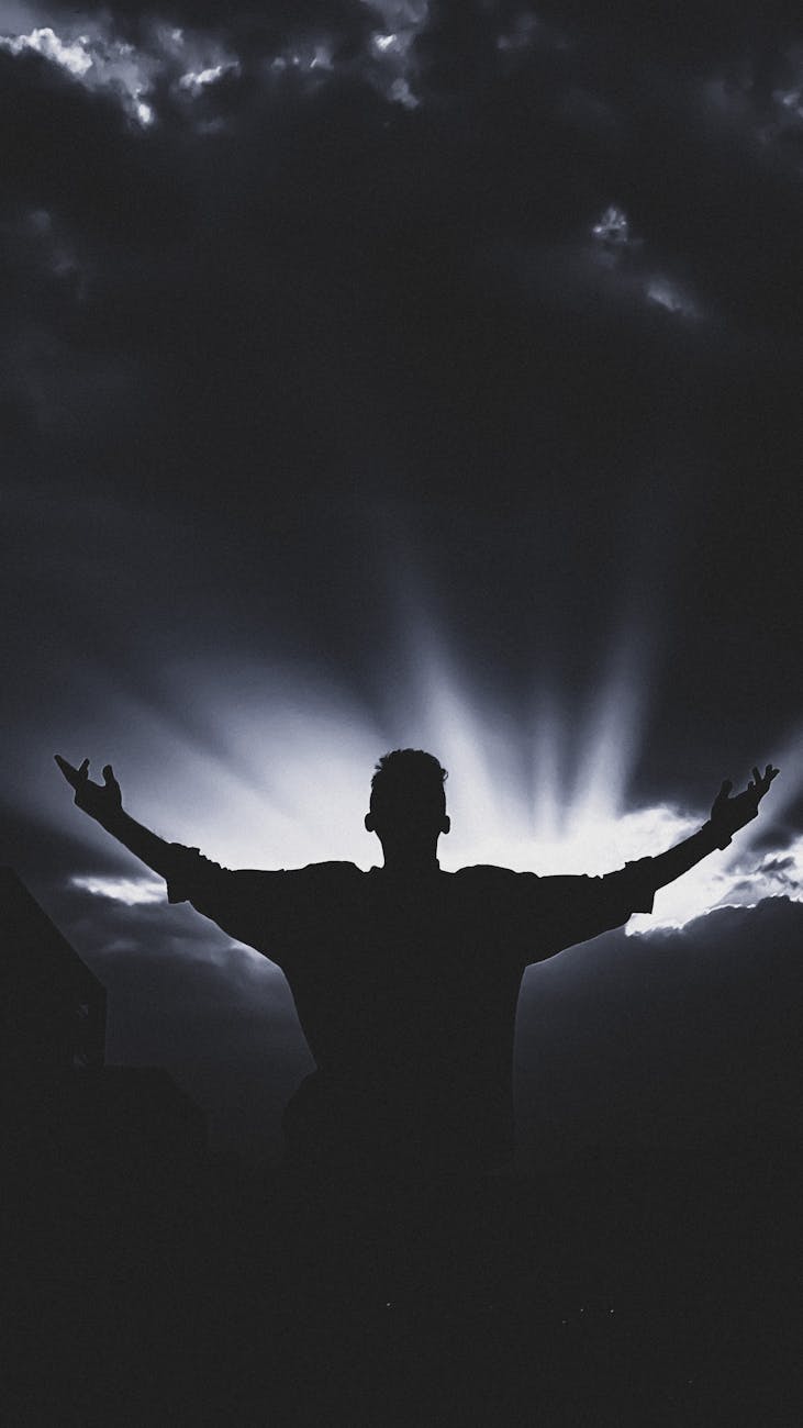 silhouette of man with open arms against dramatic sunset